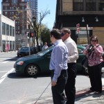 Gentleman under blindfold waiting to cross to street with O&M instructor